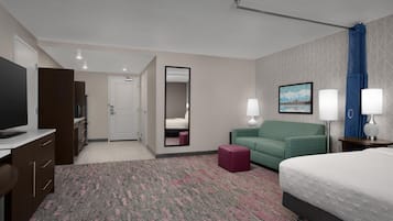 Una habitación de hotel con una cama, un escritorio con televisor, un sofá verde, un espejo y dos lámparas de noche.