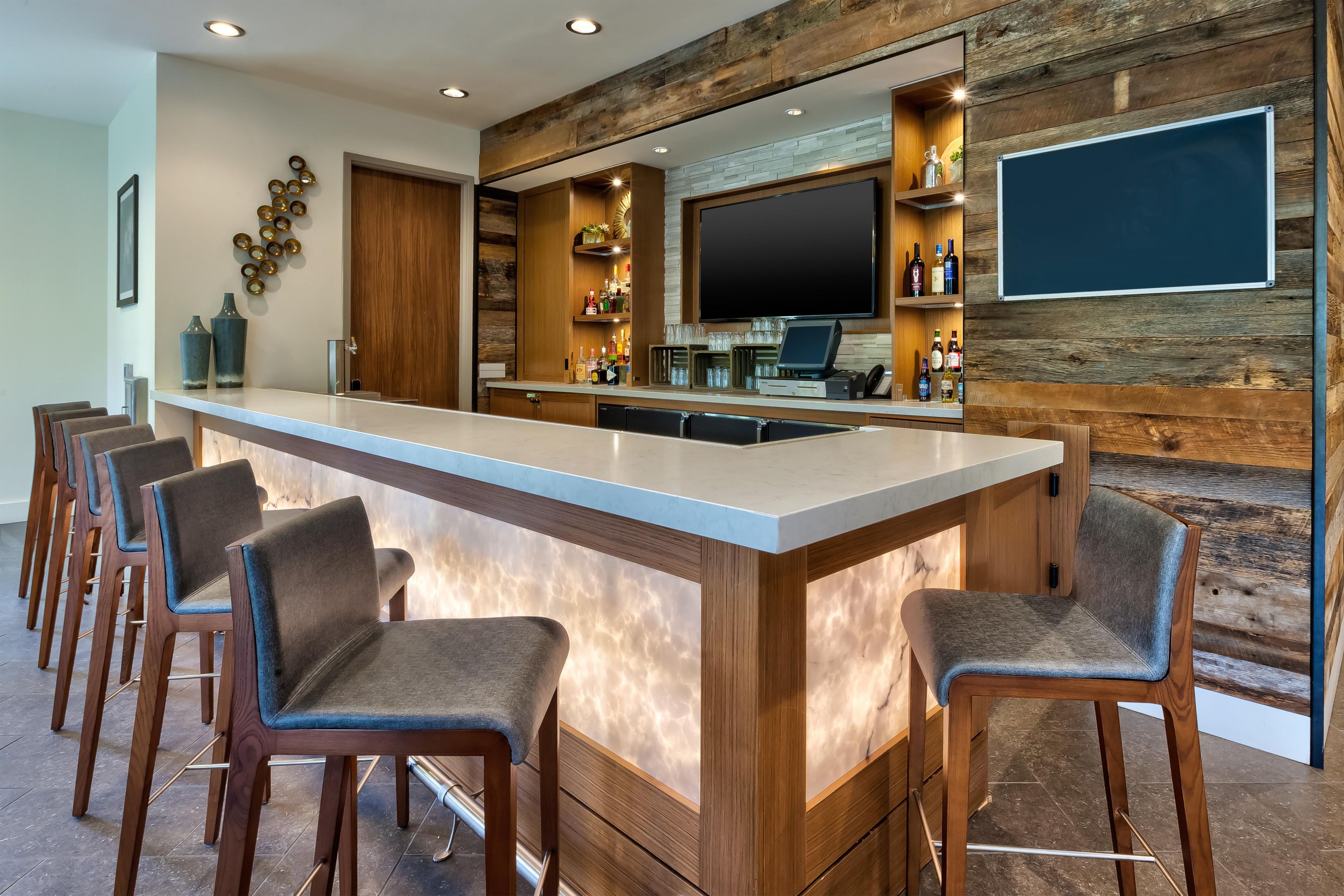A bar area with a long counter, multiple bar stools, a television, and shelves with bottles.