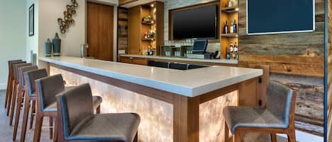 A bar area with a long counter, multiple bar stools, a television, and shelves with bottles.