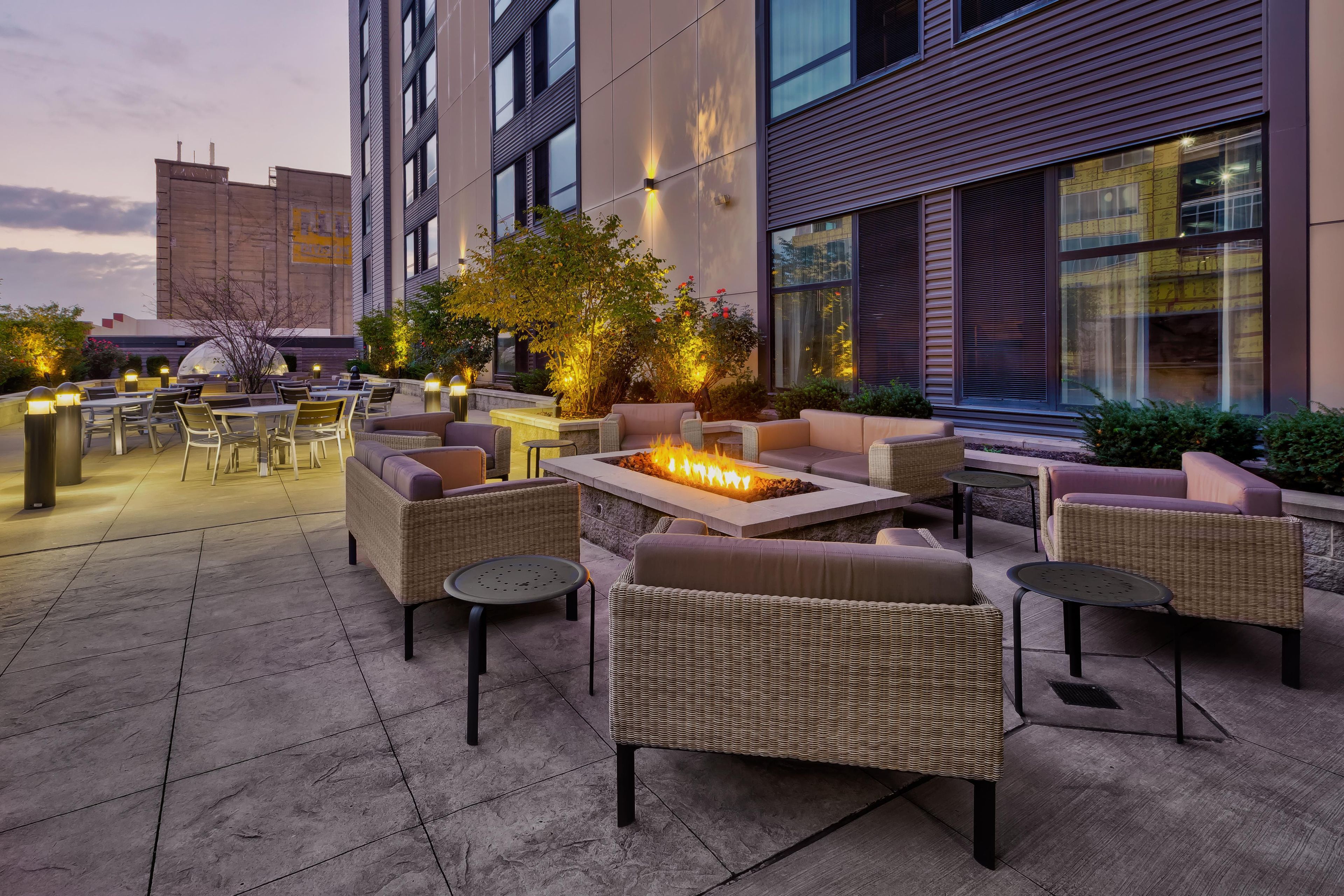 An outdoor seating area with wicker furniture, a fire feature, and a view of the building's exterior.