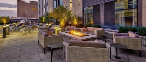 An outdoor seating area with wicker furniture, a fire feature, and a view of the building's exterior.