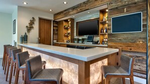 A bar area with a marble countertop, wooden bar stools, and a television mounted on the wall.