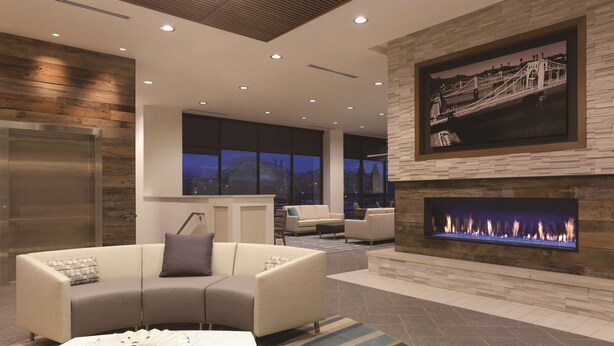 A modern living room with a fireplace, sofas, and a large window overlooking a cityscape at night.