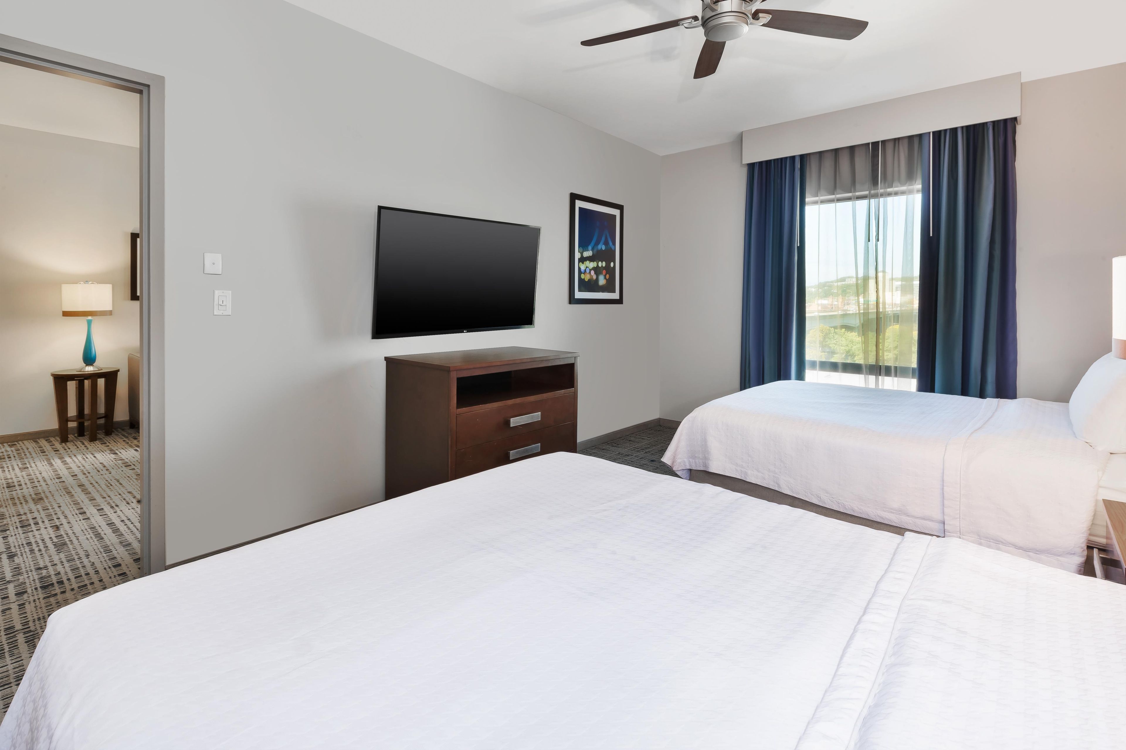 A hotel room with two beds, a flat-screen TV, a ceiling fan, a night view poster, and a window with curtains.