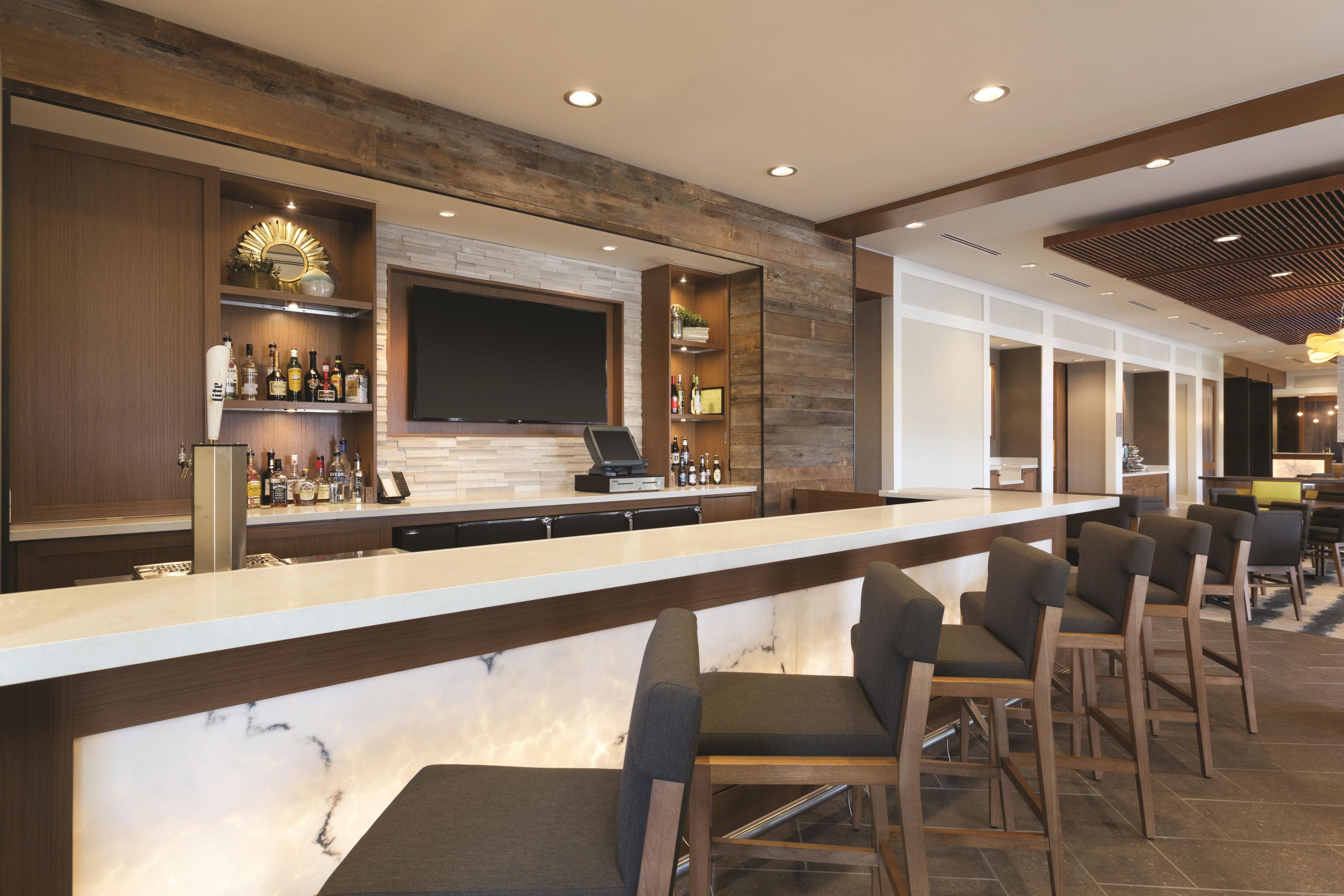 A bar area with a long counter, bar stools, a flat-screen TV mounted on the wall, and shelves with bottles.