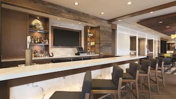 A bar area with a long counter, bar stools, a flat-screen TV mounted on the wall, and shelves with bottles.