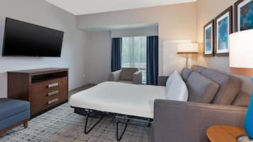 A hotel room with a bed, a desk, a TV, a lamp, and a window with curtains.