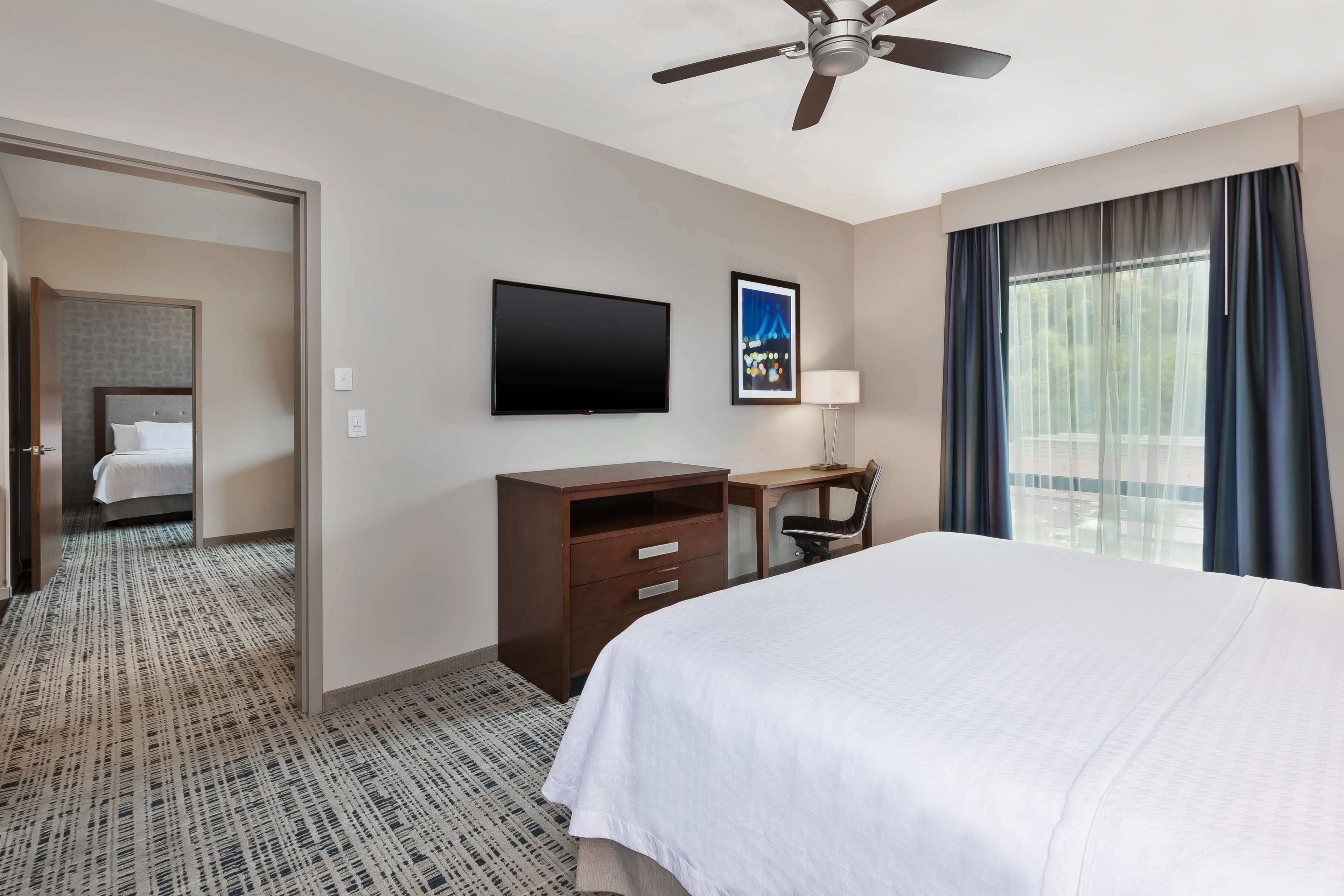 A hotel room with a bed, a desk, a chair, a television, and a window with curtains.
