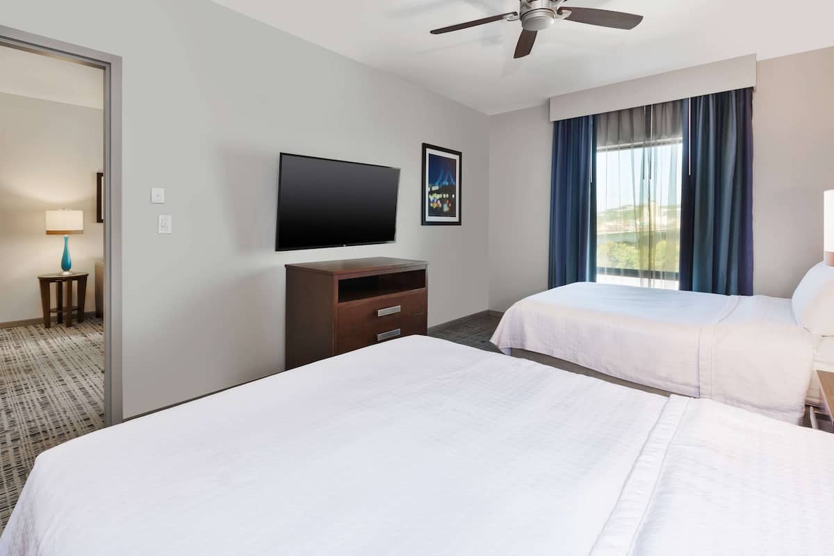 Een hotelkamer met twee bedden, een flatscreen-tv, een plafondventilator en een raam met gordijnen.
