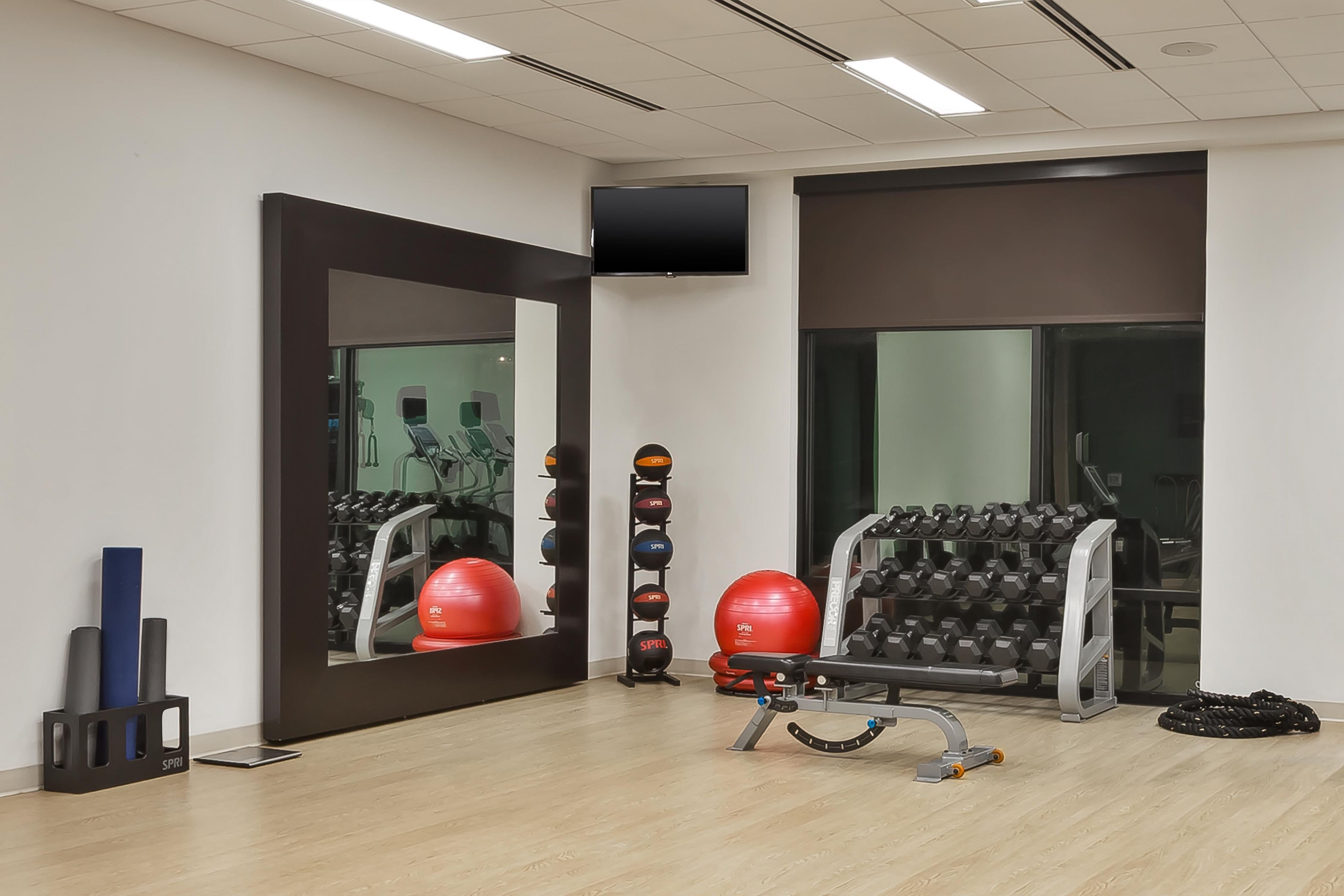 A gym with exercise equipment, a mirror, and a television on the wall.