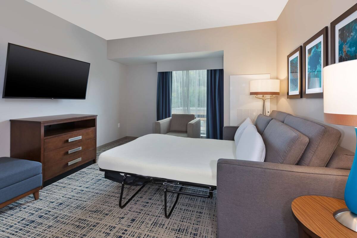 Een hotelkamer met een bed, een bank, een televisie, een bureau en een raam met gordijnen.