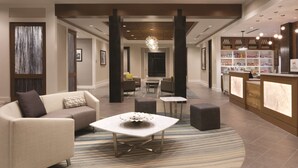 A hotel lobby with a reception desk, seating area, and a large chandelier.