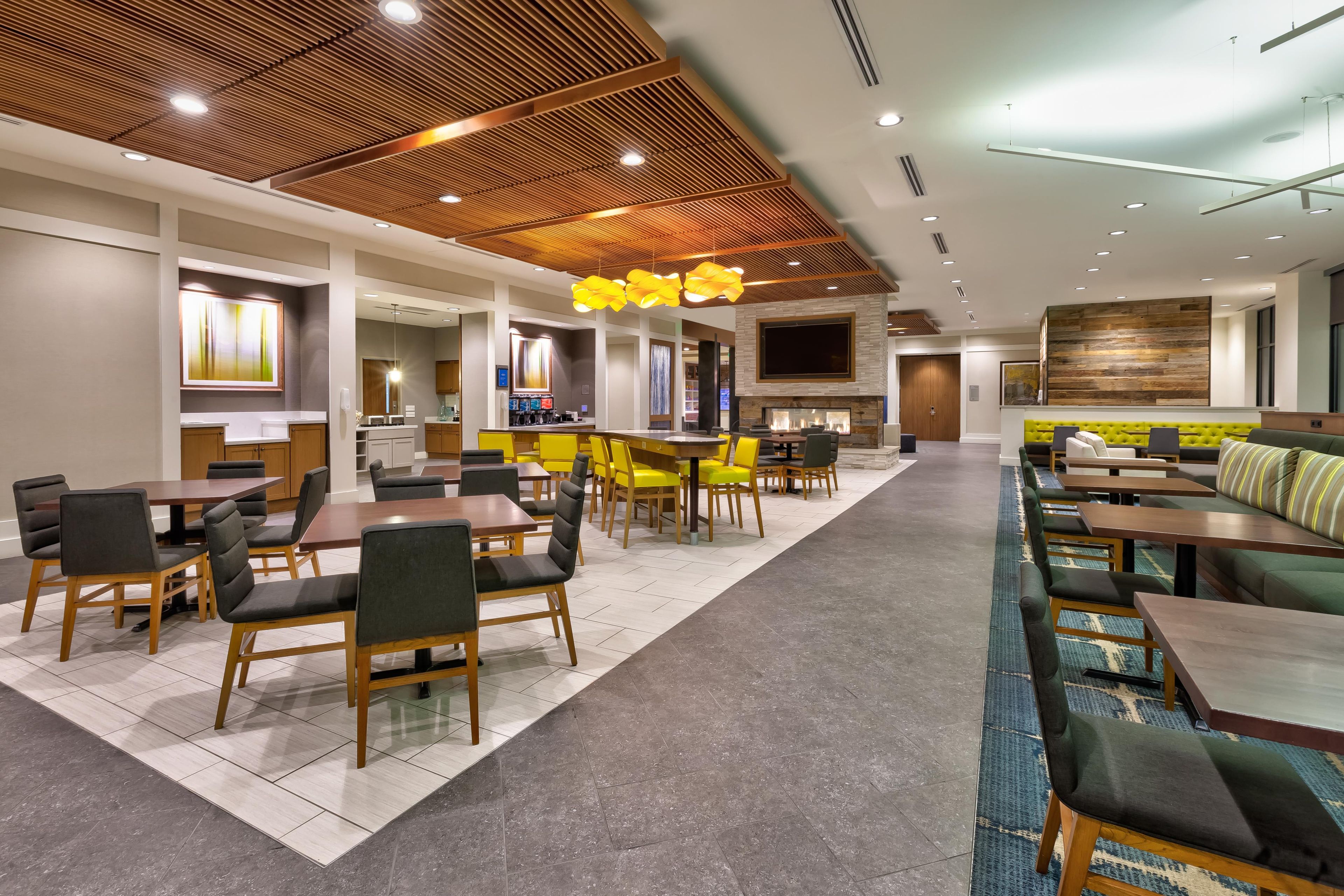 A modern hotel lobby with a bar area, seating arrangements, and a fireplace.