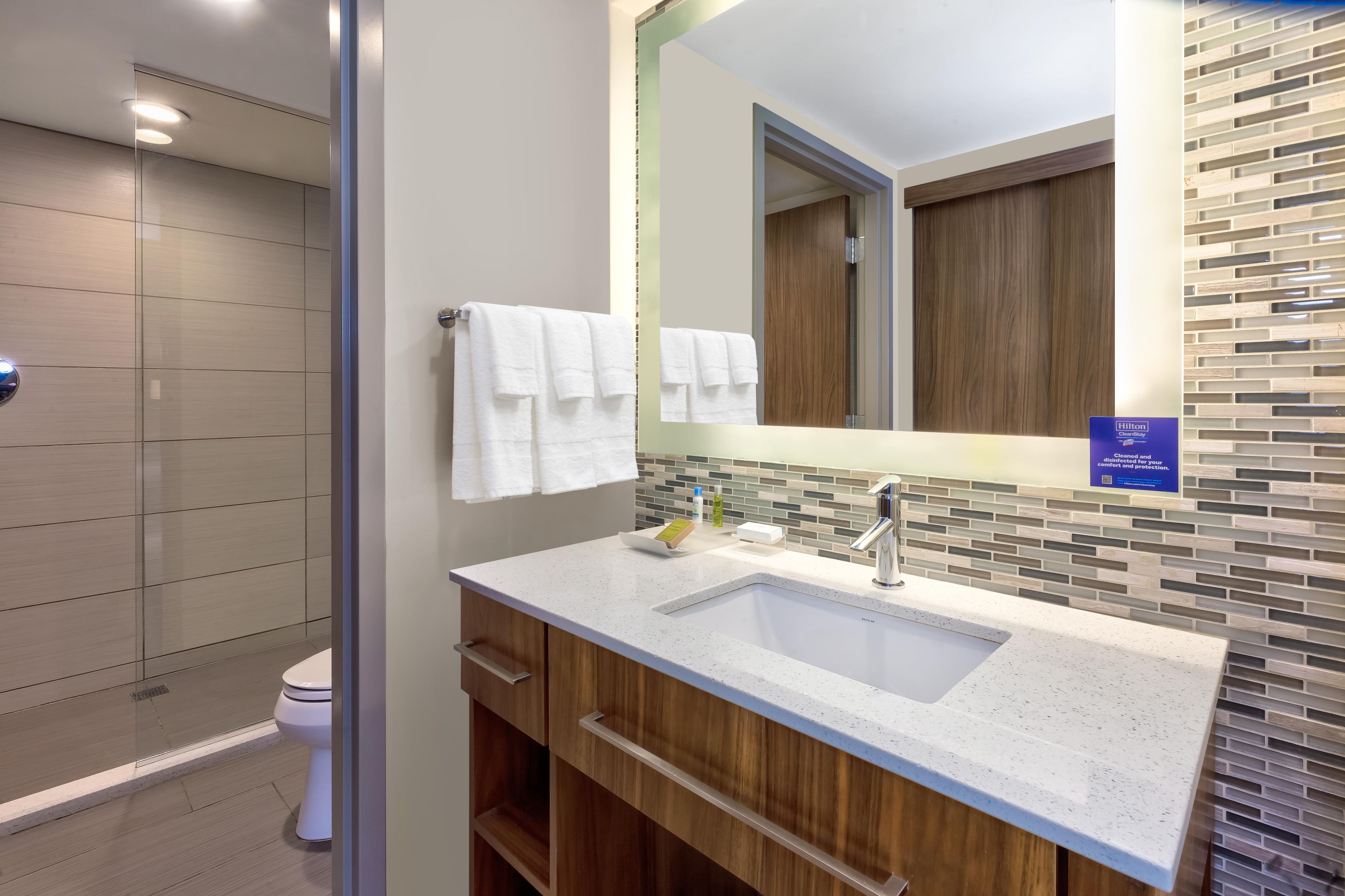 A modern bathroom with a glass shower enclosure, a white sink with a large mirror, and wooden cabinetry.