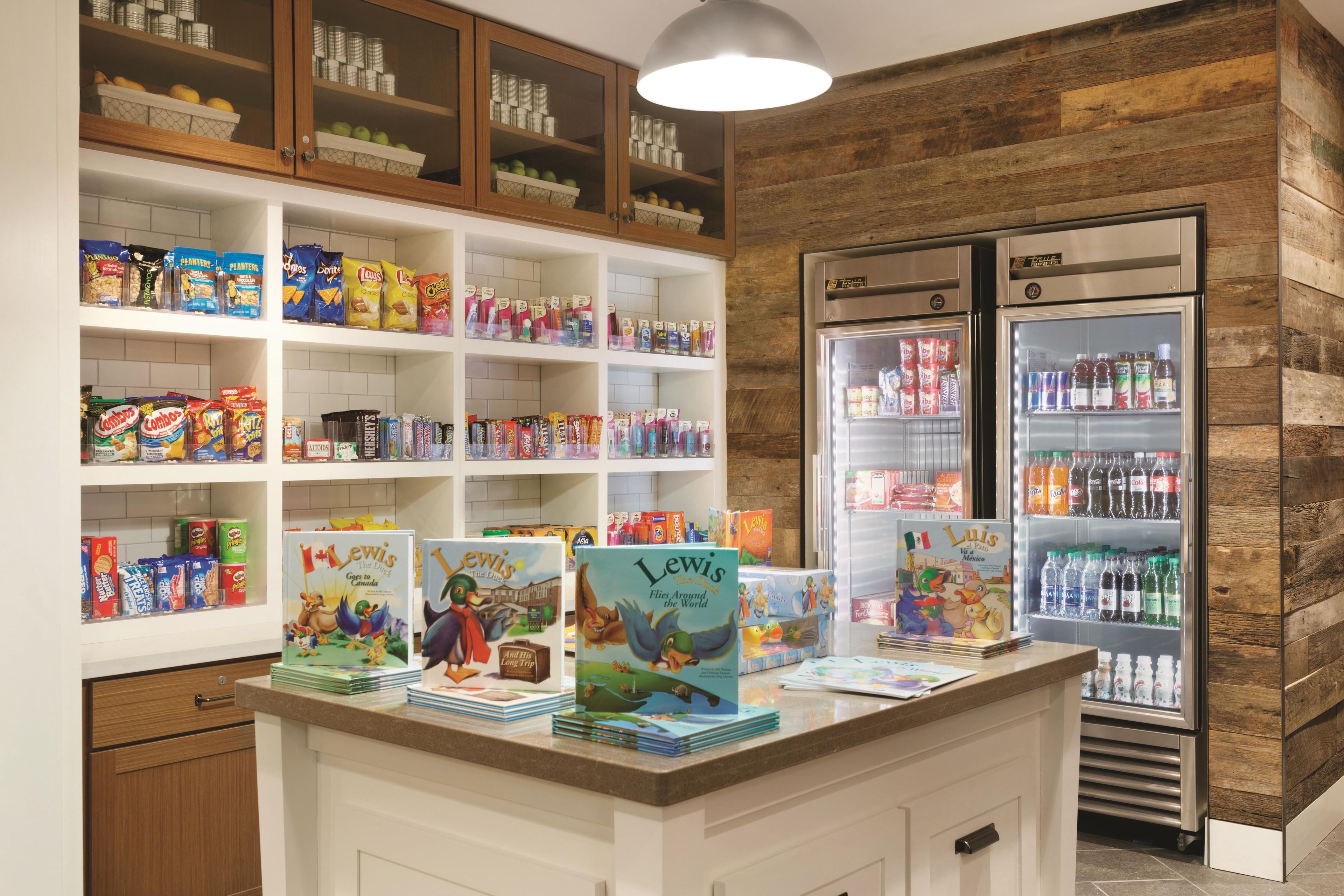 Espaço infantil com corredores de lanches, balcão refrigerado e uma mesa com livros.
