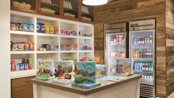 Espaço infantil com corredores de lanches, balcão refrigerado e uma mesa com livros.