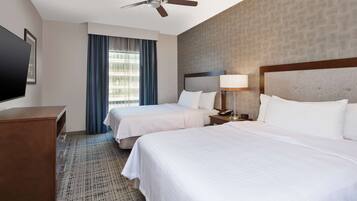 A hotel room with two beds, a ceiling fan, a TV, and a window with curtains.