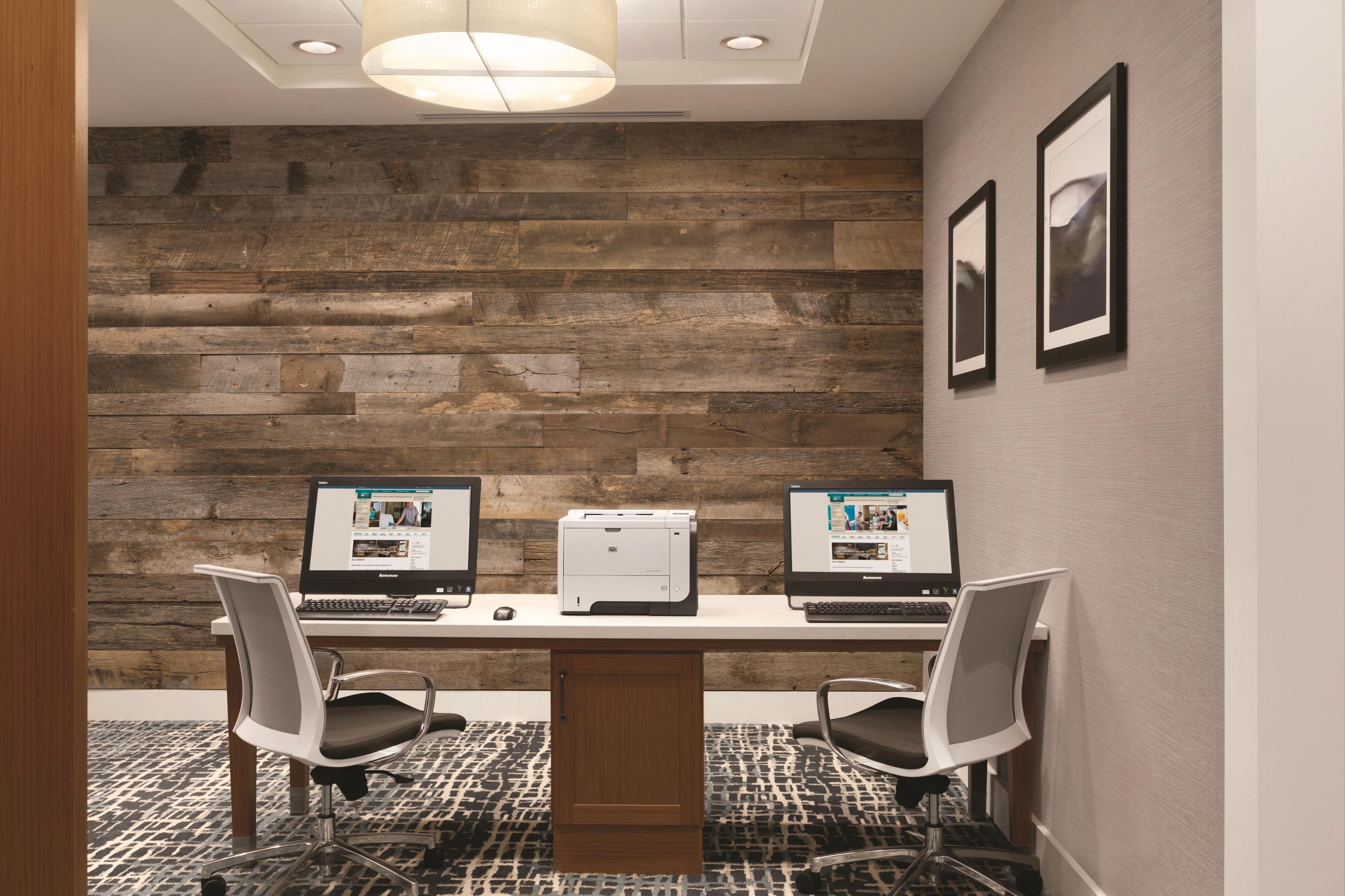 A conference room with a wooden wall, two desks with computers, chairs, and a printer.