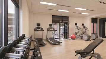 Uma academia com esteiras, elípticos, um banco de musculação e um remo.