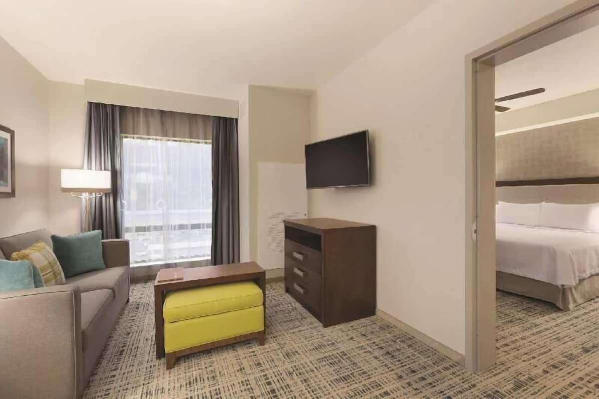 Een hotelkamer met een bed, een televisie, een bureau met lades, een bank en een raam met gordijnen.