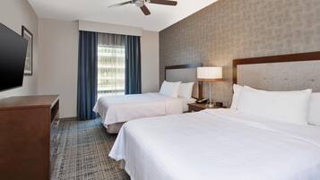 A hotel room with two beds, a ceiling fan, a TV, and a window with curtains.