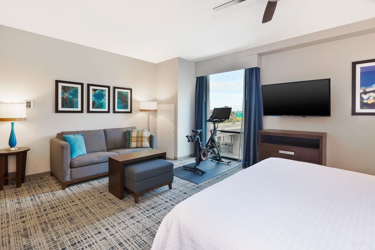 Een hotelkamer met een bed, een bank, een bureau, een televisie en een hometrainer.