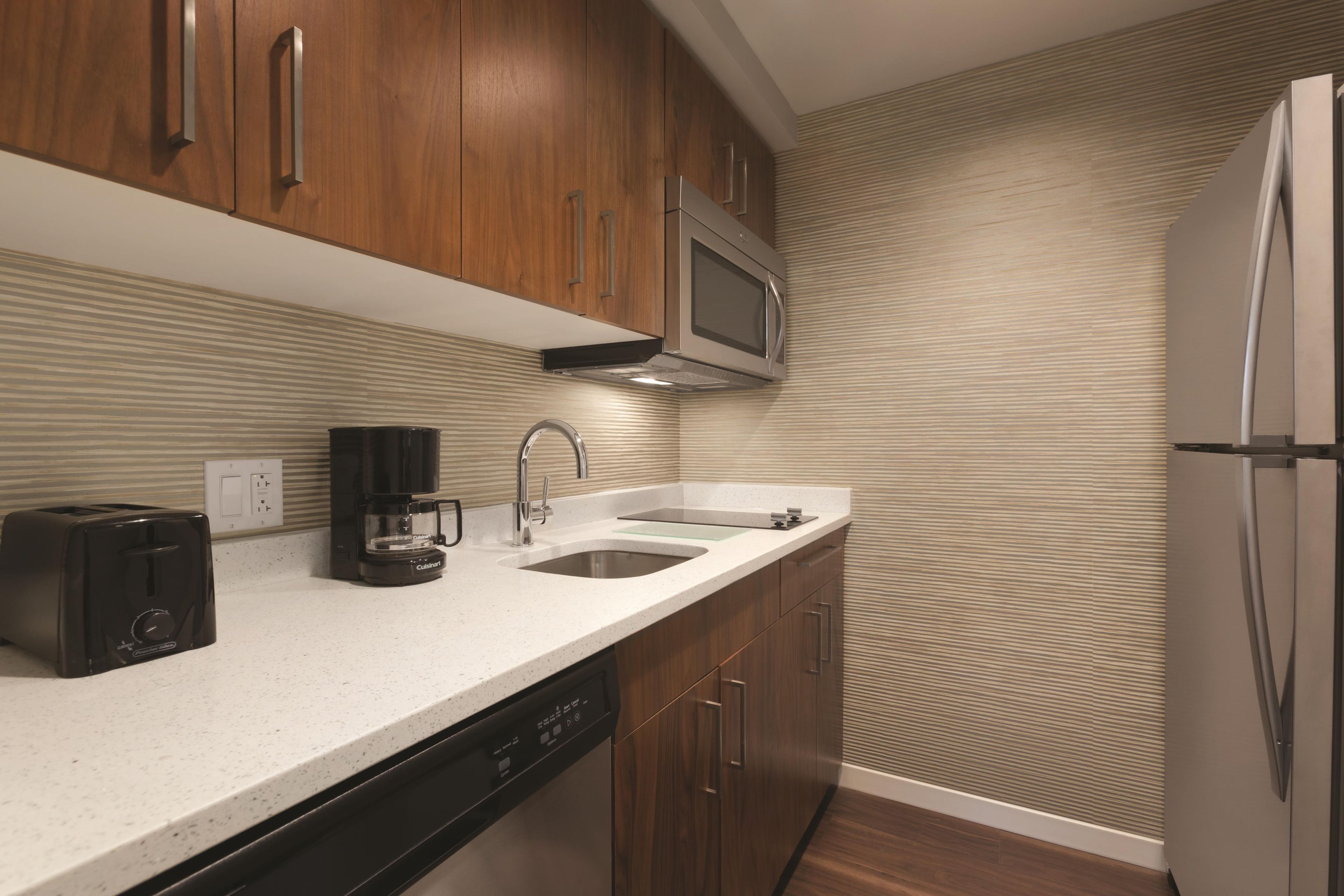 A modern kitchen with wooden cabinets, a stainless steel microwave, a coffee maker, a dishwasher, and a refrigerator.