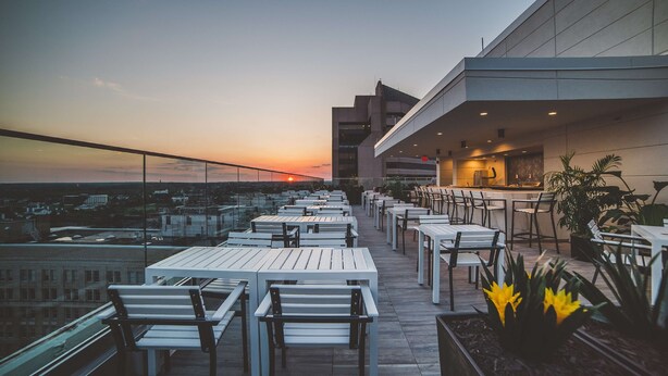 Une terrasse extérieure avec des tables et des chaises blanches, un espace bar et une vue sur le coucher de soleil.