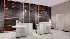 Un espace d’accueil avec deux comptoirs de réception blancs, un mur en briques sombres avec un motif en réseau, et une porte sur la droite.