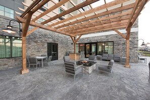 Patio esterno con pavimento in pietra, pergola in legno e disposizione dei posti a sedere.