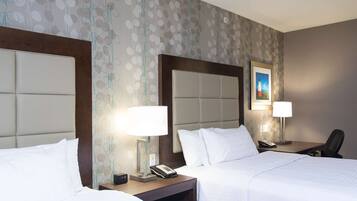 A hotel room with two beds, nightstands with lamps, a desk with a chair, and a painting on the wall.