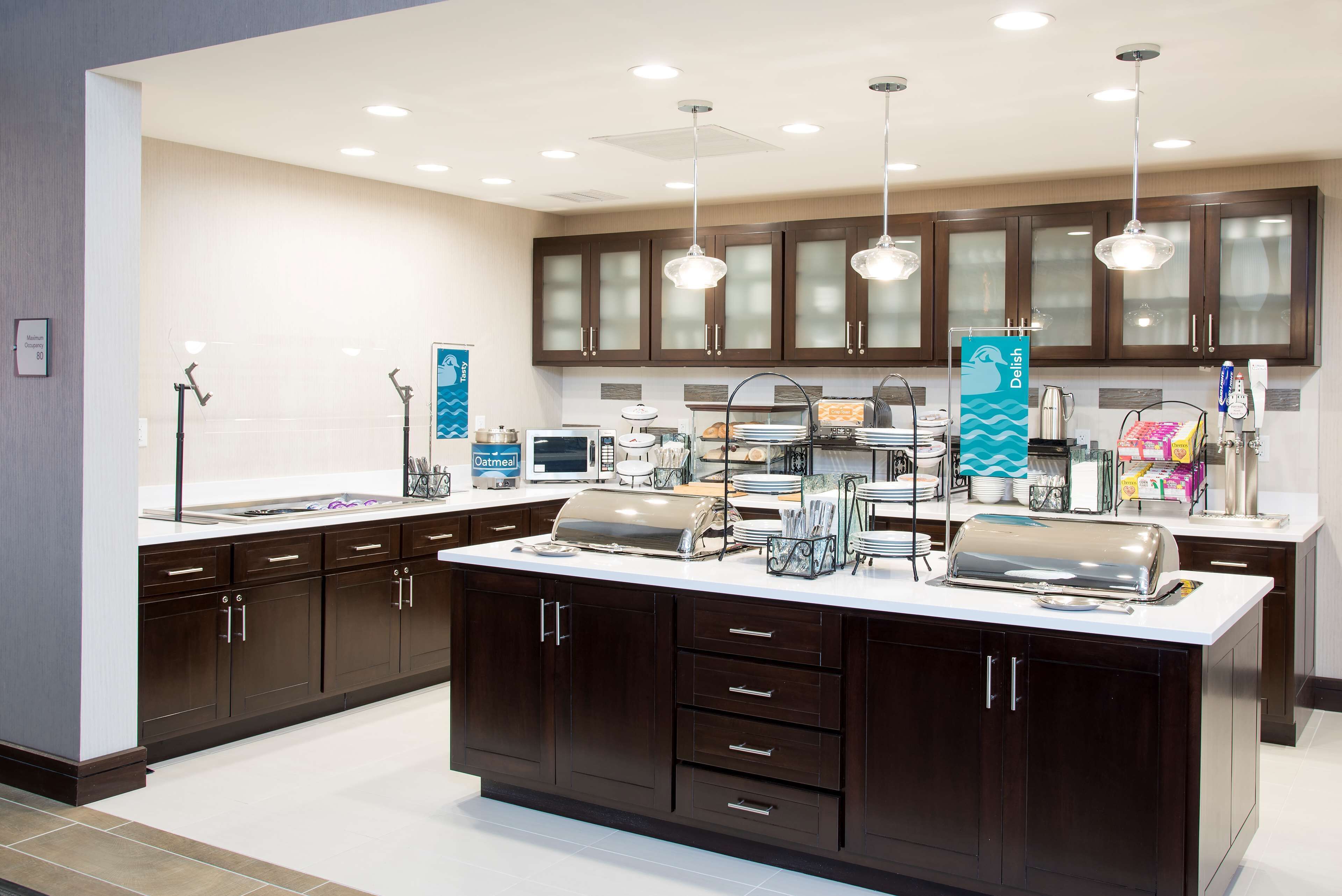 A modern kitchen with dark wooden cabinets, a central island with a built-in grill, and overhead pendant lighting.