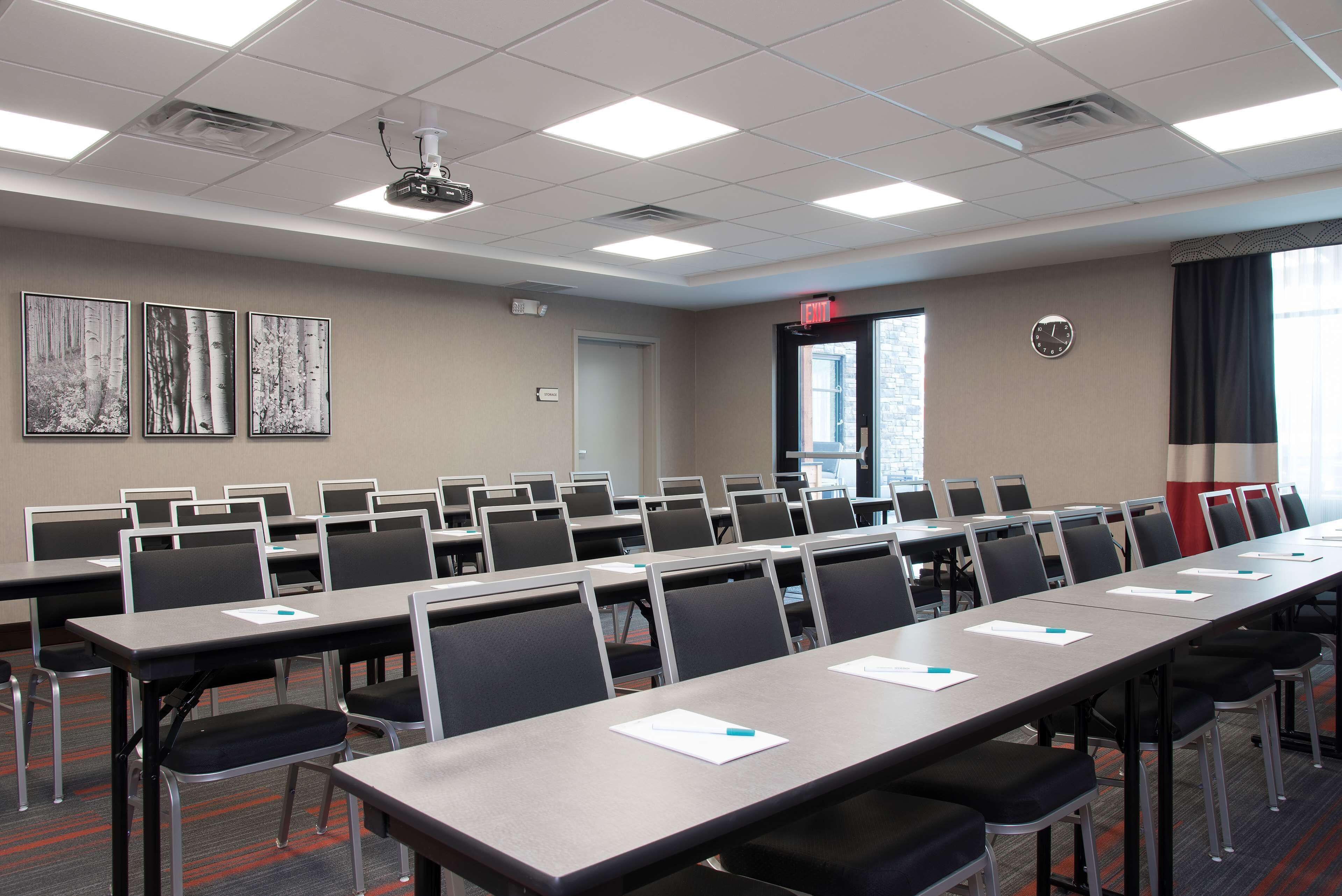 A conference room with long tables, chairs, and a projector on the ceiling.