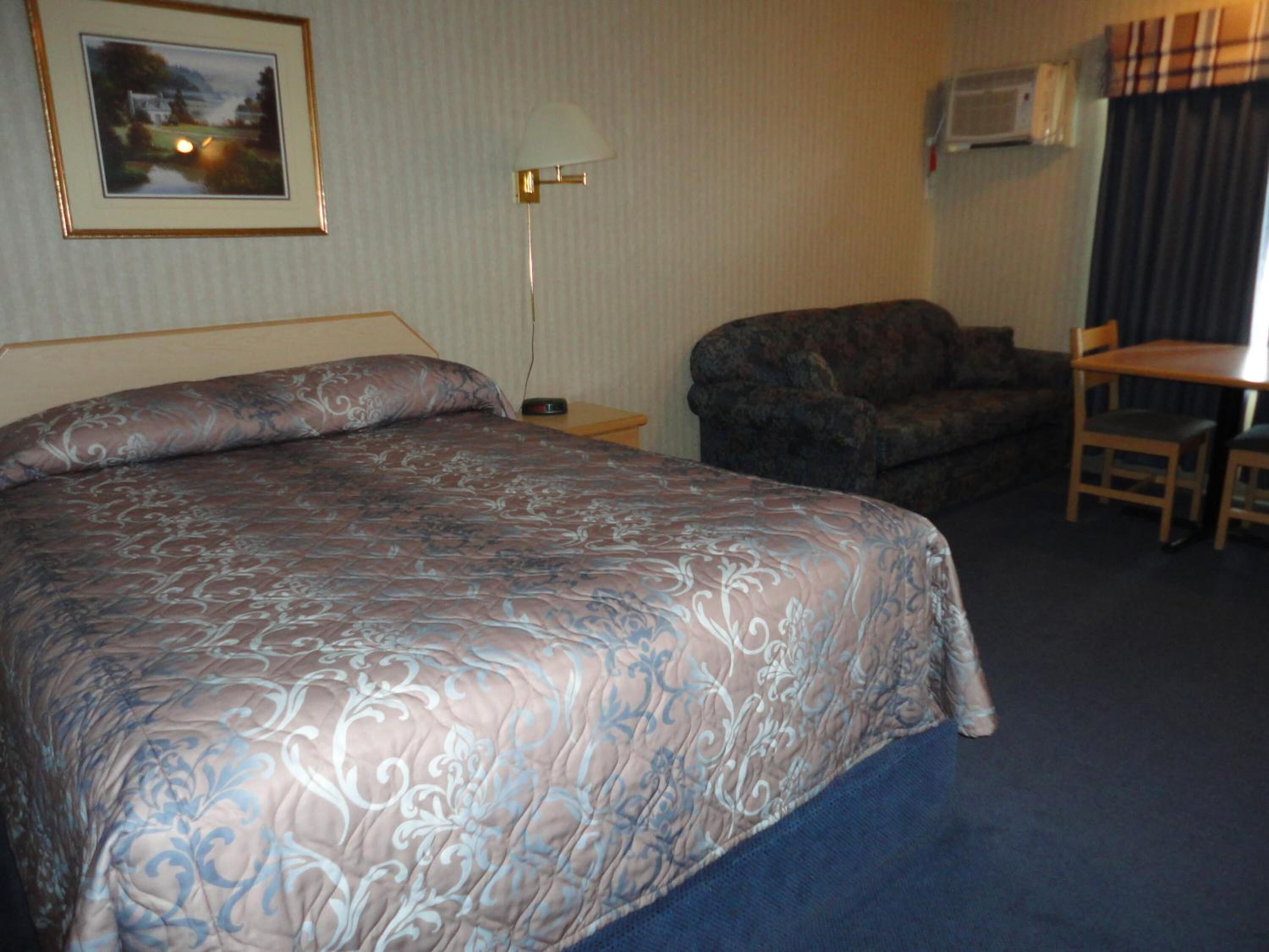 Une chambre d’hôtel avec un grand lit, un canapé, une petite table, une lampe et un appareil de climatisation.