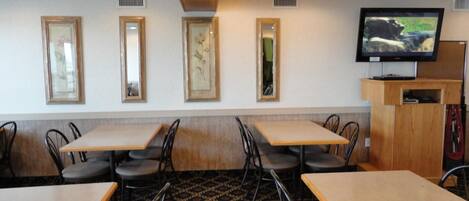 A dining area with tables and chairs, a television mounted on a wooden stand, and framed artwork on the wall.