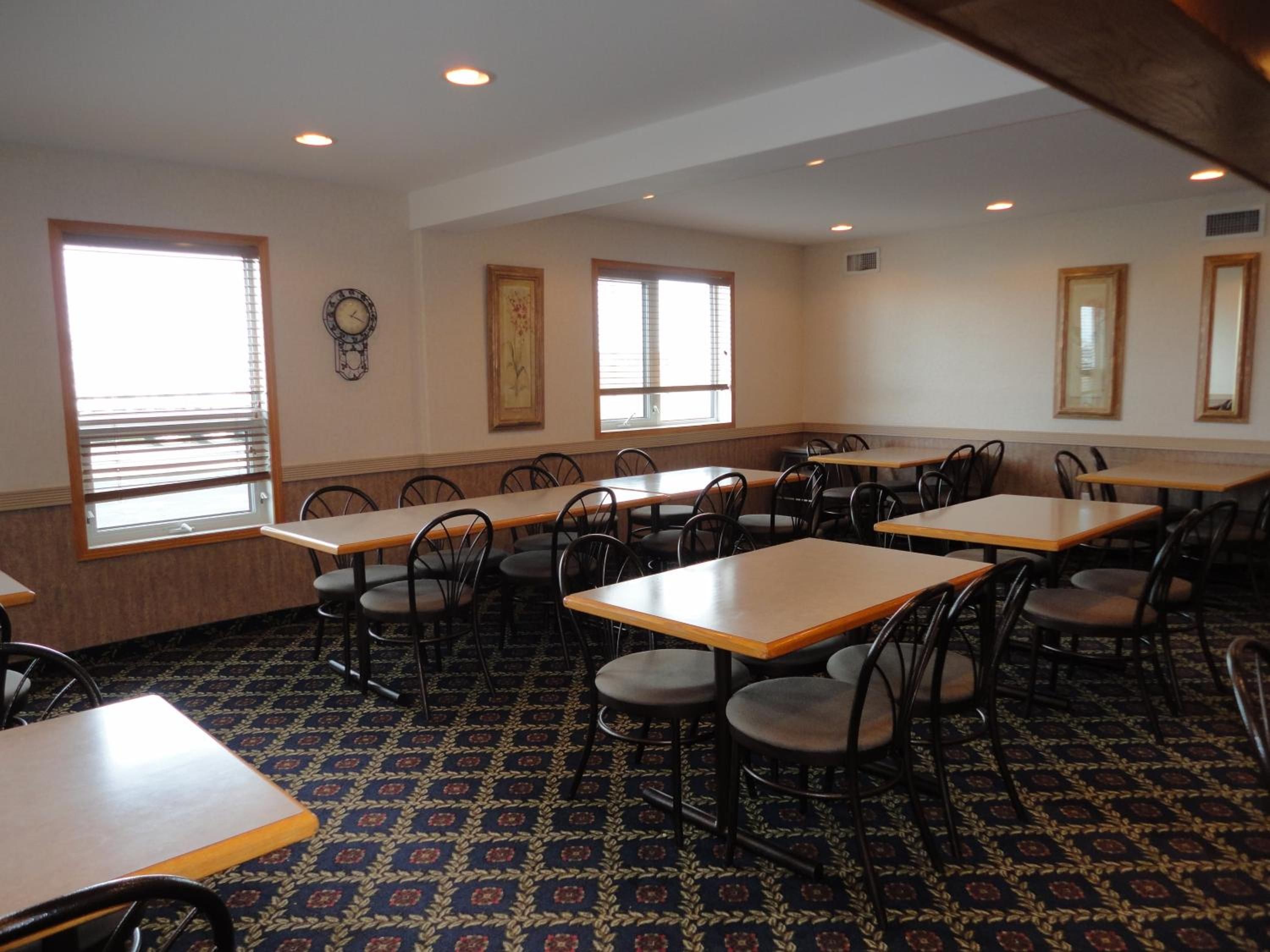 Comedor con varias mesas y sillas, ventanas amplias y alfombra estampada.