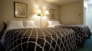 A hotel room with two beds, each with a patterned bedspread, two wall-mounted lamps, and two framed floral paintings. - Perfect Inns & Suites (Weyburn)