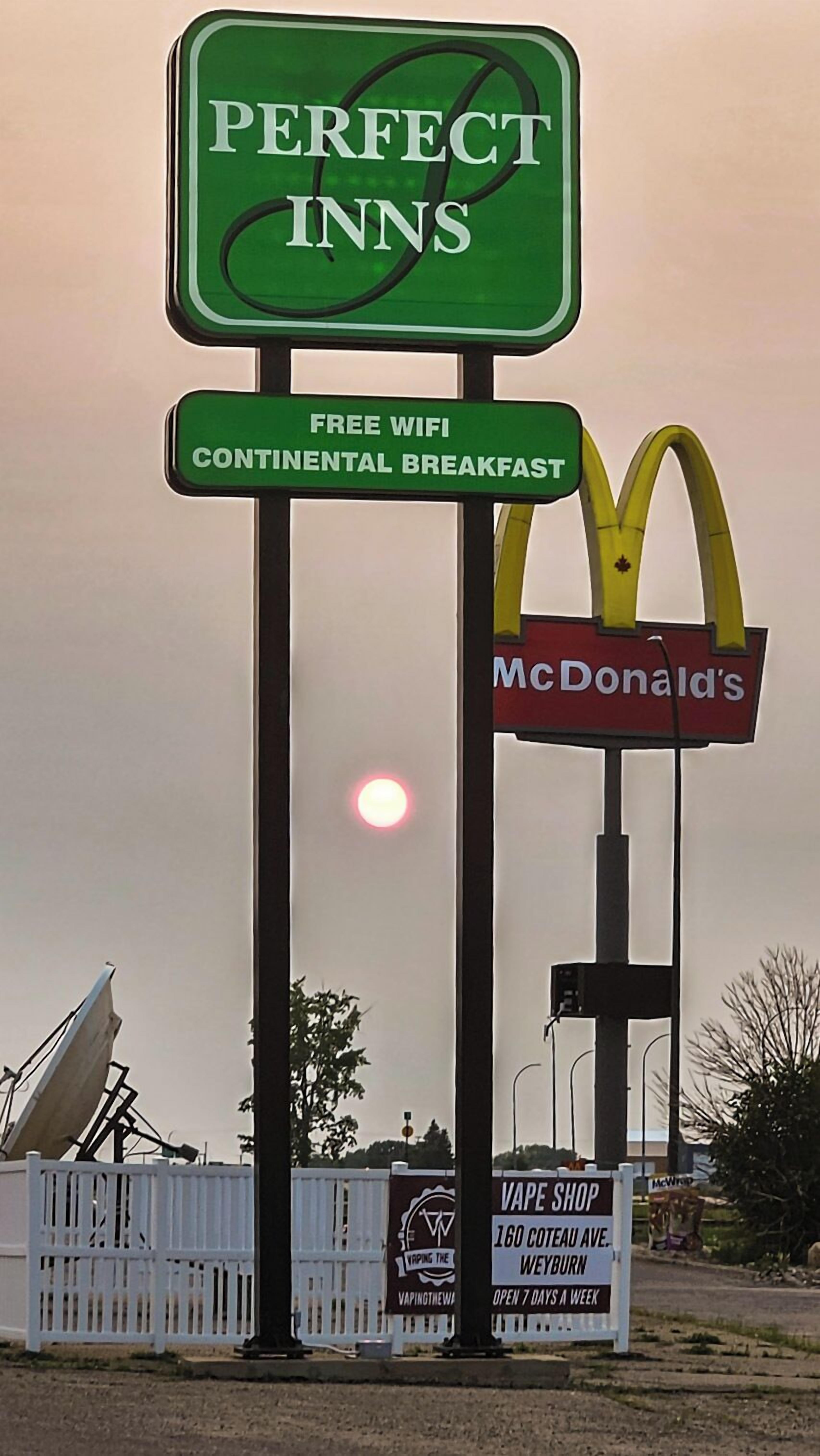 Une enseigne pour la chaîne d’hôtels Perfect Inns, avec le logo de McDonald’s en dessous, et une enseigne de magasin de cigarettes électroniques en arrière-plan.
