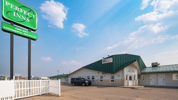A motel with a green roof, a signboard for Perfect Inns, and a car parked in front.