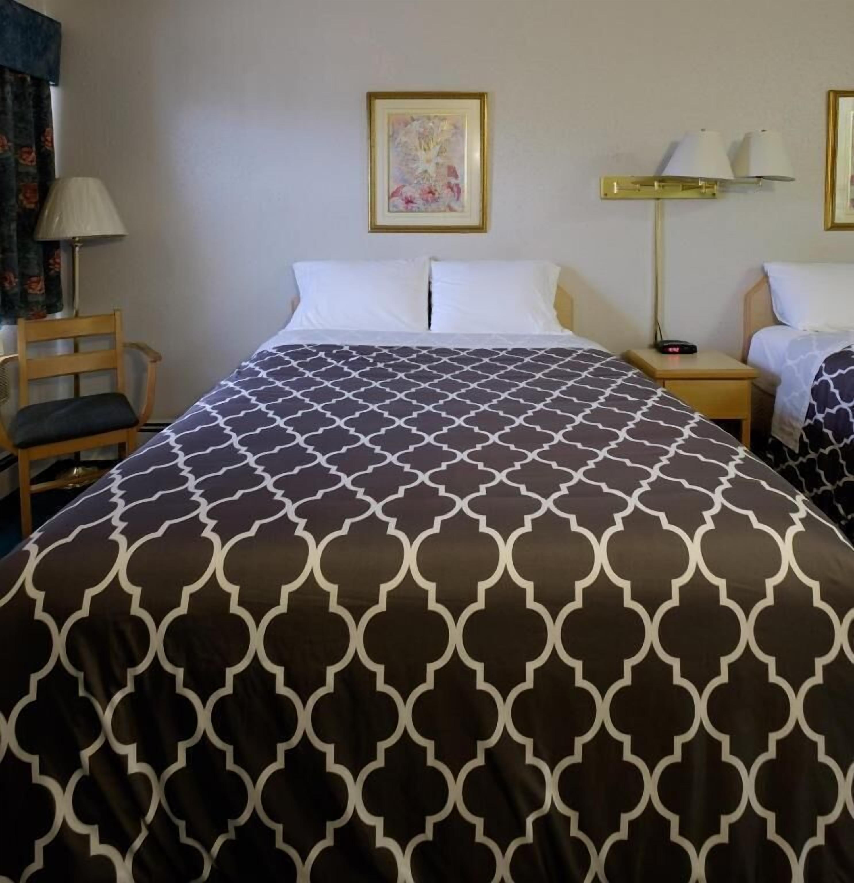 Habitación de hotel con una cama grande, una mesita de noche, una silla, una lámpara y un cuadro en la pared.