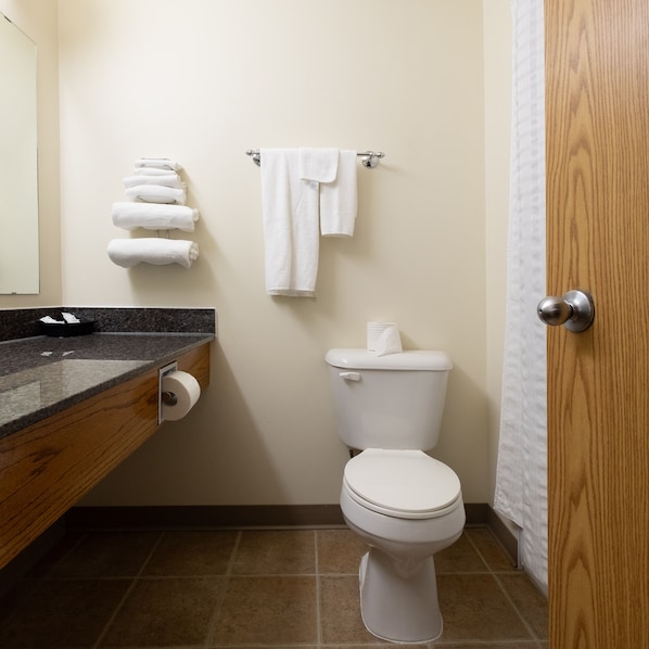 A bathroom with a toilet, a towel rack with folded towels, a toilet paper holder, and a wooden door.