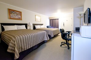 A hotel room with two beds, a desk, a chair, a television, and a door.