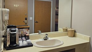 A hotel bathroom with a sink, mirror, coffee maker, and toiletries. - Perfect Inns & Suites (Weyburn)