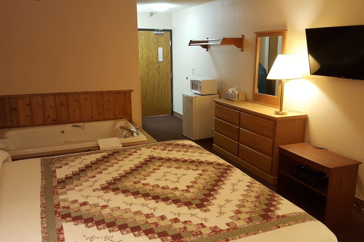 A hotel room with a bed, a bathroom, a dresser, a TV, and a lamp.