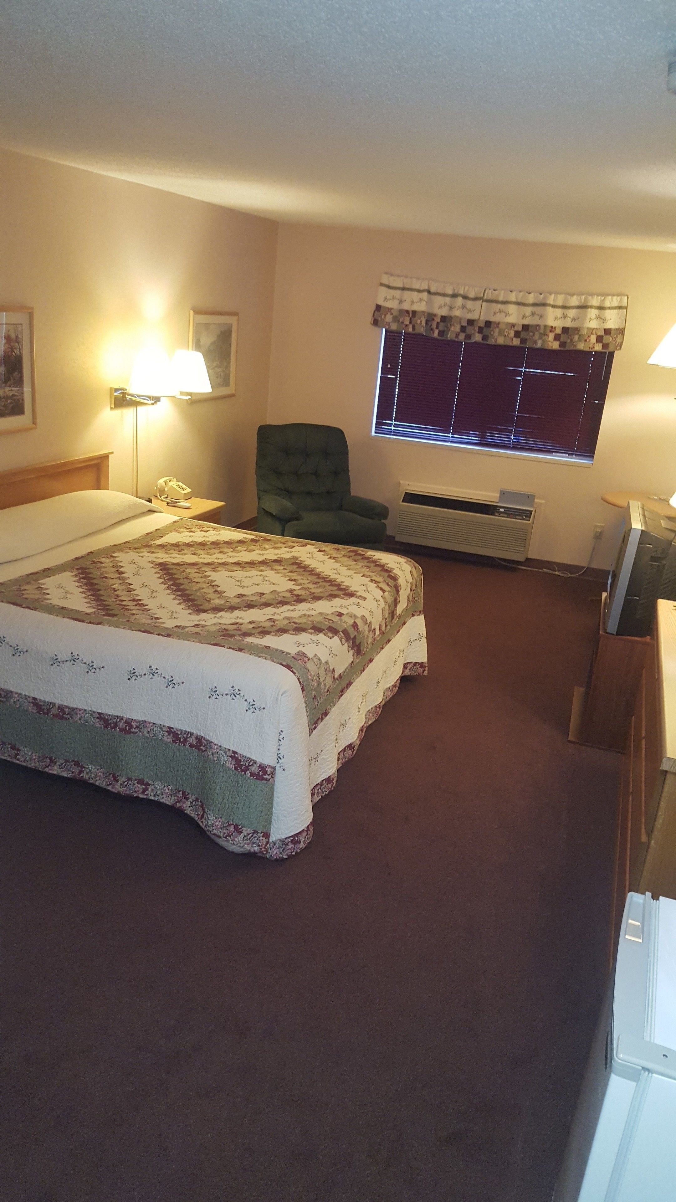 A bedroom with a large bed, a chair, a desk, and a window with blinds.