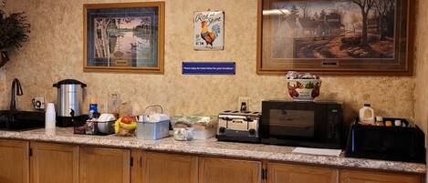 A kitchen with wooden cabinets, a granite countertop, a coffee maker, a toaster, a microwave, and a framed picture of a rural scene.