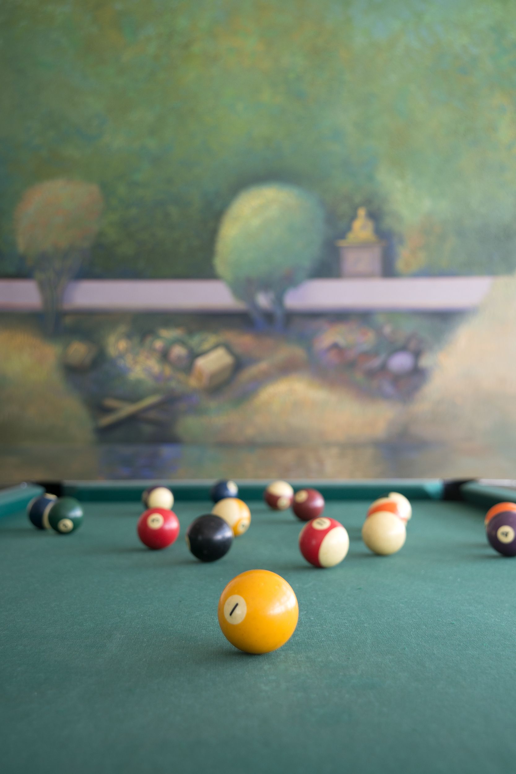 A pool table with various colored balls and a painting in the background.