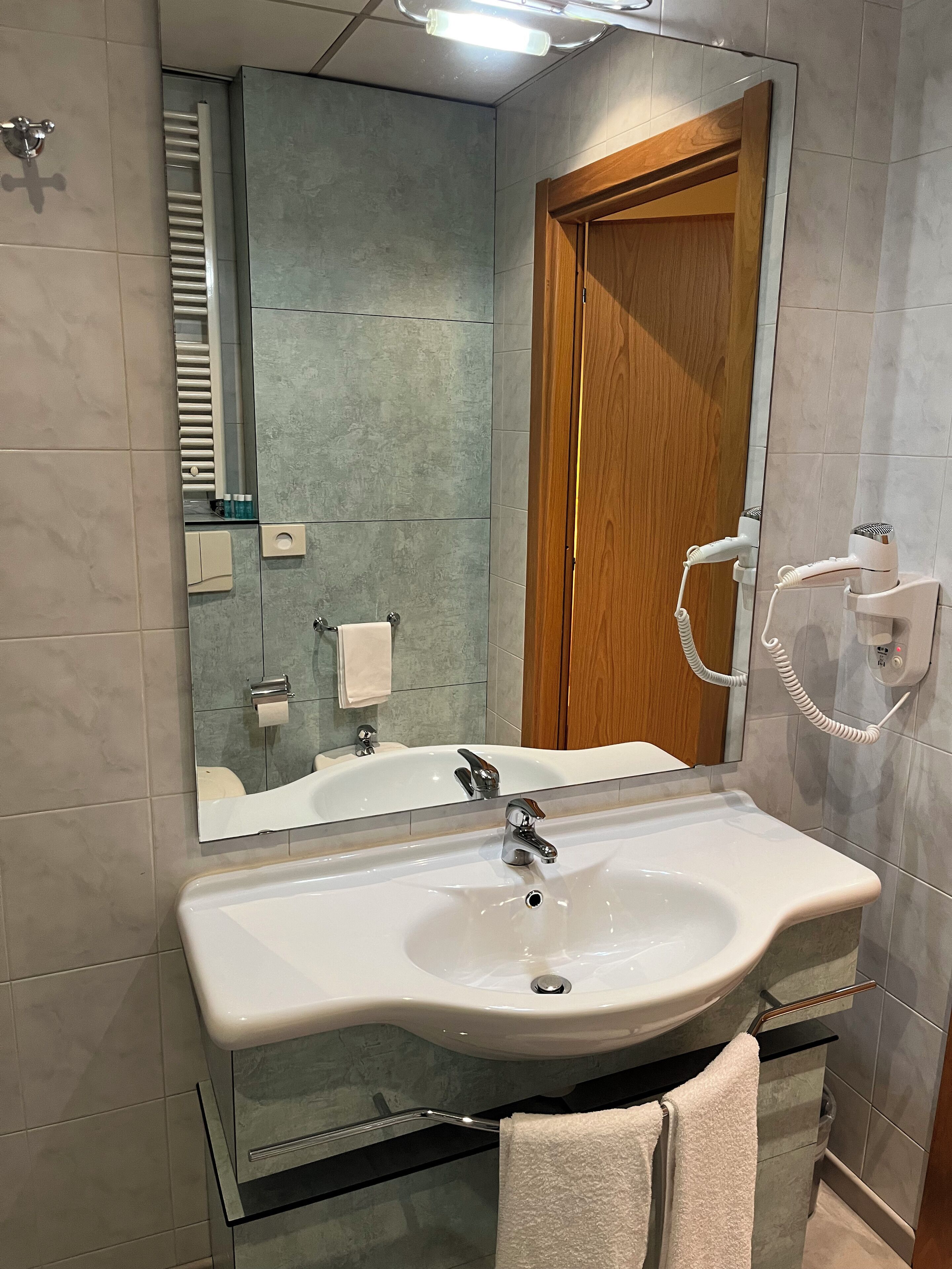 Un baño moderno con un espejo grande, un lavabo y un secador de pelo.