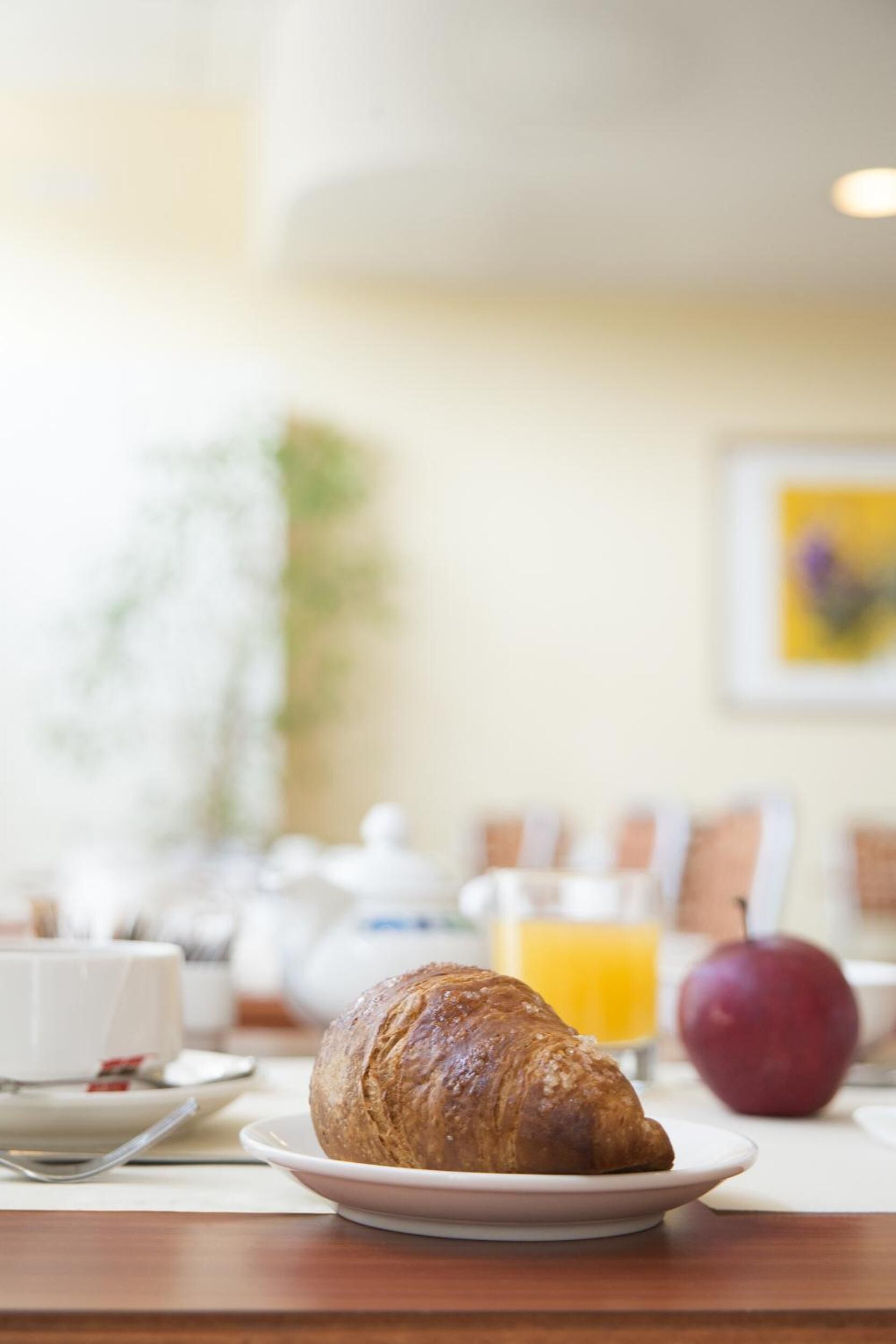 Ein Frühstückstisch mit einem Croissant auf einem Teller, einem Glas Orangensaft und einem Apfel.