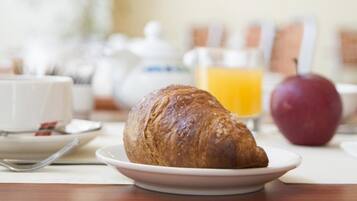 Ein Frühstückstisch mit einem Croissant auf einem Teller, einem Glas Orangensaft und einem Apfel.